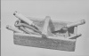 Schwarz-weiß-Fotografie einer Holzkiste, die eine Kneifzange und weitere Werkzeuge enthält.