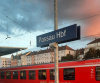 Blaues Schild, auf dem "Passau Hbf" steht vor einem roten Zug und einem orangen Wolkenhimmel.